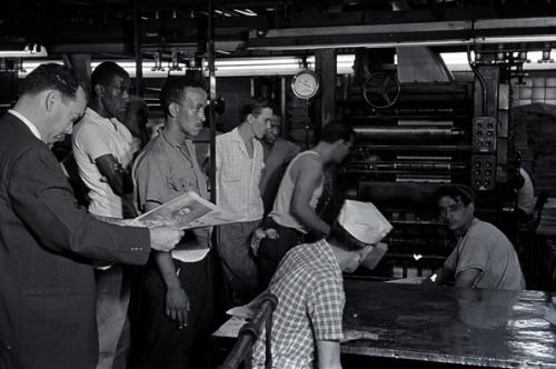 A la izquierda el primer director de Granma, Isidoro Malmierca, revisa el primer número del diario rodeado de un grupo de trabajadores.